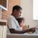 Side view of young Black father reading a book with his little daughter while sitting on the couch
